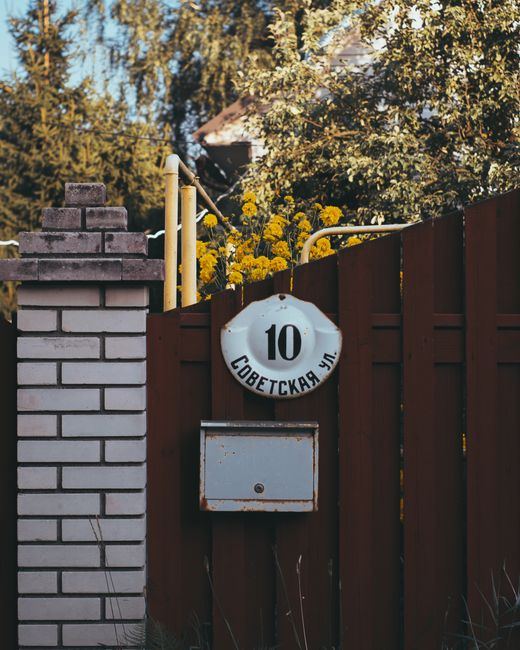 A close-up view of a residential outdoor scene featuring a dark brown wooden gate with a white circular house number sign displaying '10' and Russian text 'Советская ул.', mounted above a s
